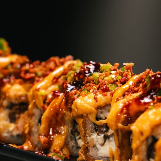 Torched sushi rolls under spicy mayo and eel sauce, on a black studio ground