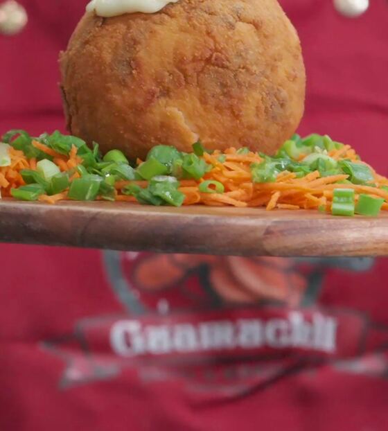 A cook in a red Guamuchil apron pours sauce over a fried roll